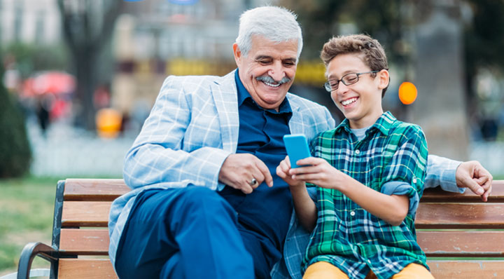 Man and boy sitting on park bench, looking at phone